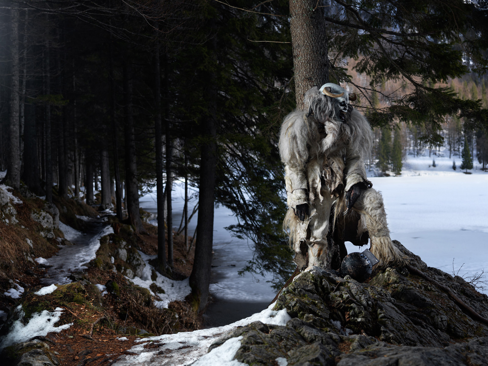 krampus si appoggia ad un albero davanti al lago ghiacciato